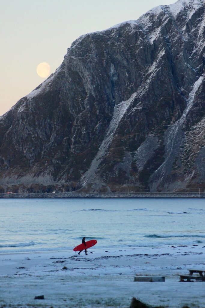 A person with a red surfboard in front of a mountain